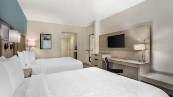 A hotel room with two beds, a desk, a chair, a TV mounted on the wall, and a door leading to another room.