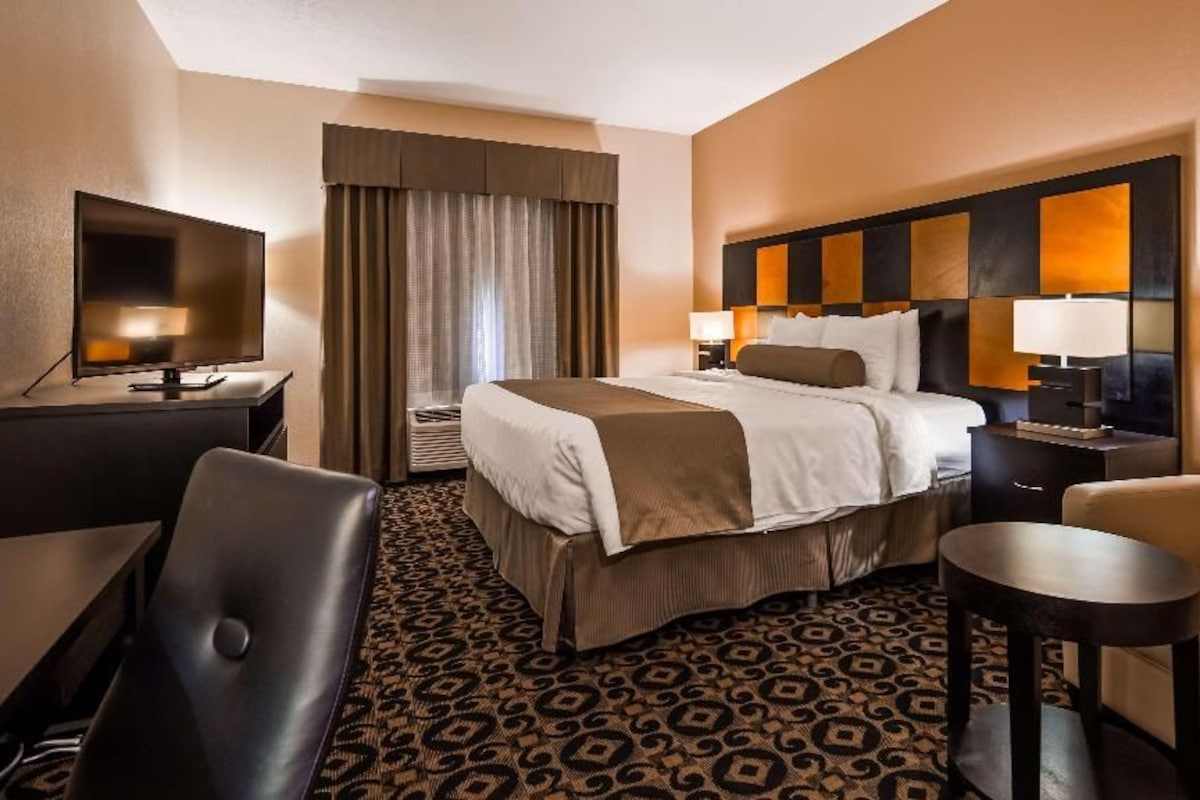 Une chambre d’hôtel avec un lit, un bureau, une chaise, une télévision et une lampe.
