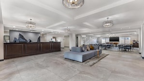 A spacious hotel lobby with a reception desk, seating area, and a dining space.