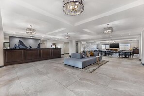 A spacious hotel lobby with a reception desk, seating area, and a dining space.