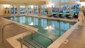 Piscina interior com água cristalina, placa indicando proibição de mergulhos e espreguiçadeiras à beira da piscina.