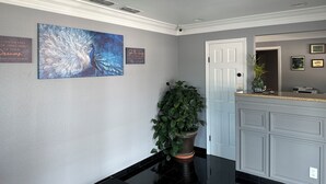 A hallway with a reception desk, a large potted plant, a wall-mounted painting, and two framed quotes. - Classic Inn Early (Early)