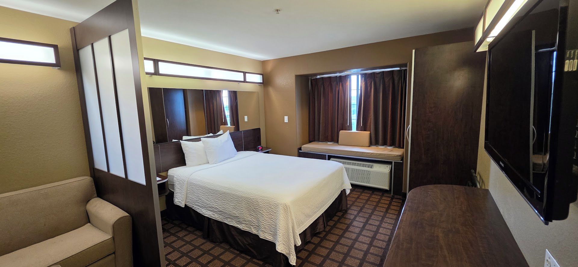 A hotel room with a bed, a desk, a chair, a wardrobe, and a window with curtains.