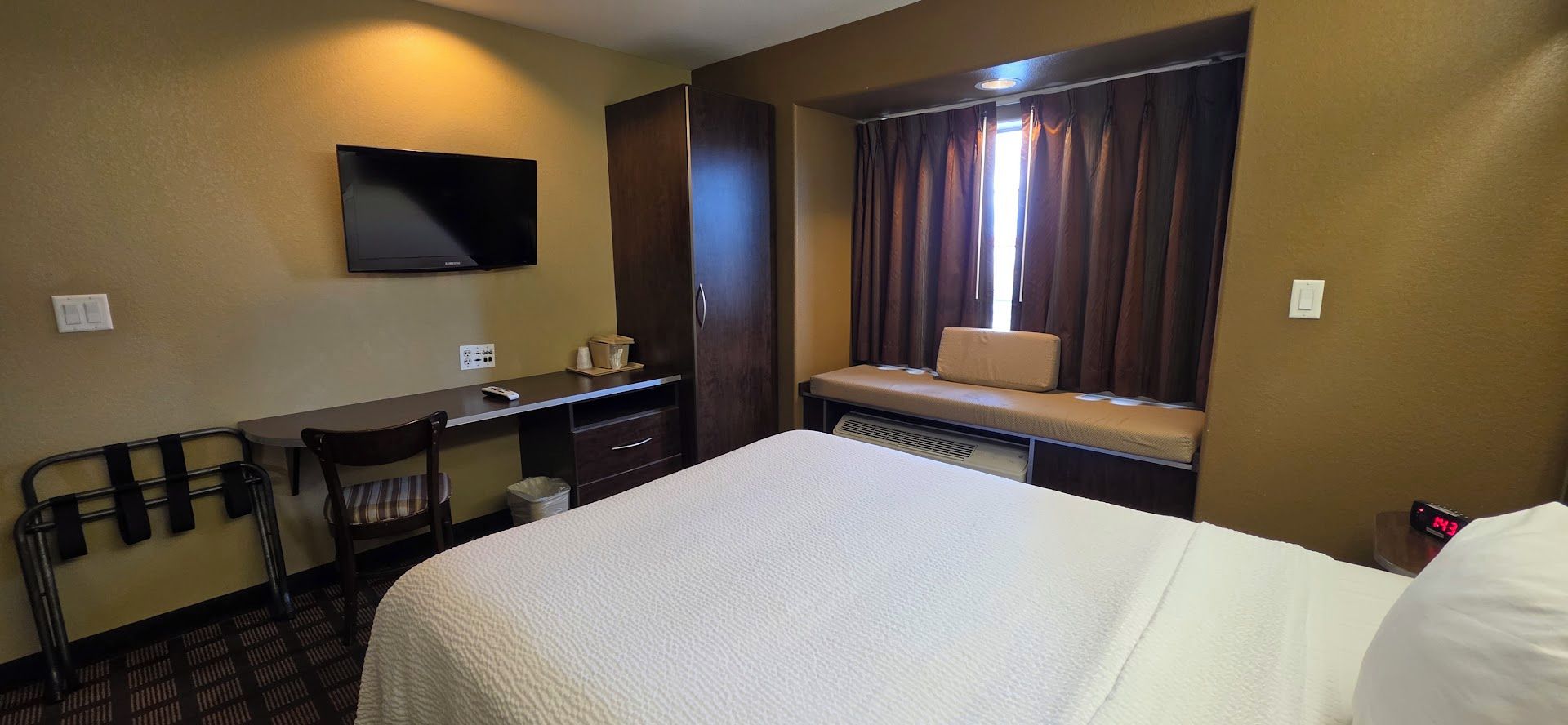 Een hotelkamer met een bed, een bureau, een stoel, een televisie en een raam met gordijnen.