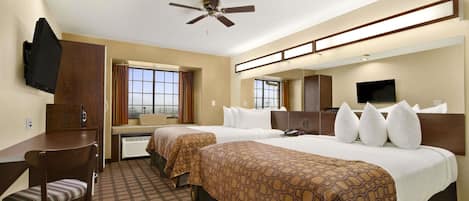 A hotel room with two beds, a desk, a chair, a television, and a ceiling fan.