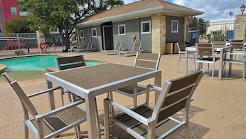 Ein Außenpoolbereich mit Tisch und Stühlen, ein kleines Gebäude mit Fenstern und einem umzäunten Pool.