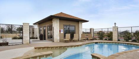 A swimming pool with a small building, likely a changing room or lounge, surrounded by a fence.