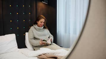 A person sitting on a bed in a room with a dark headboard, reading a book.