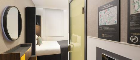 A modern hotel room with a bed, a bedside table, a mirror, a map on the wall, and a control panel.