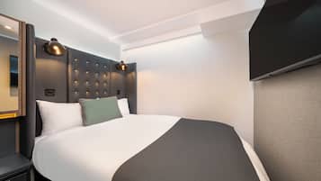 A modern hotel room with a large bed, a headboard with a light fixture, a flat-screen TV, and a bedside table.