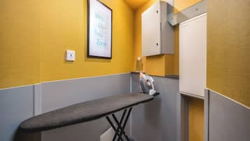 Une petite pièce avec un fer à repasser gris, un panneau encadré accroché au mur et un meuble blanc.
