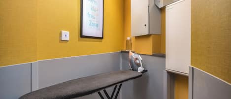 A compact room with a grey ironing board, a framed sign on the wall, and a white cabinet.