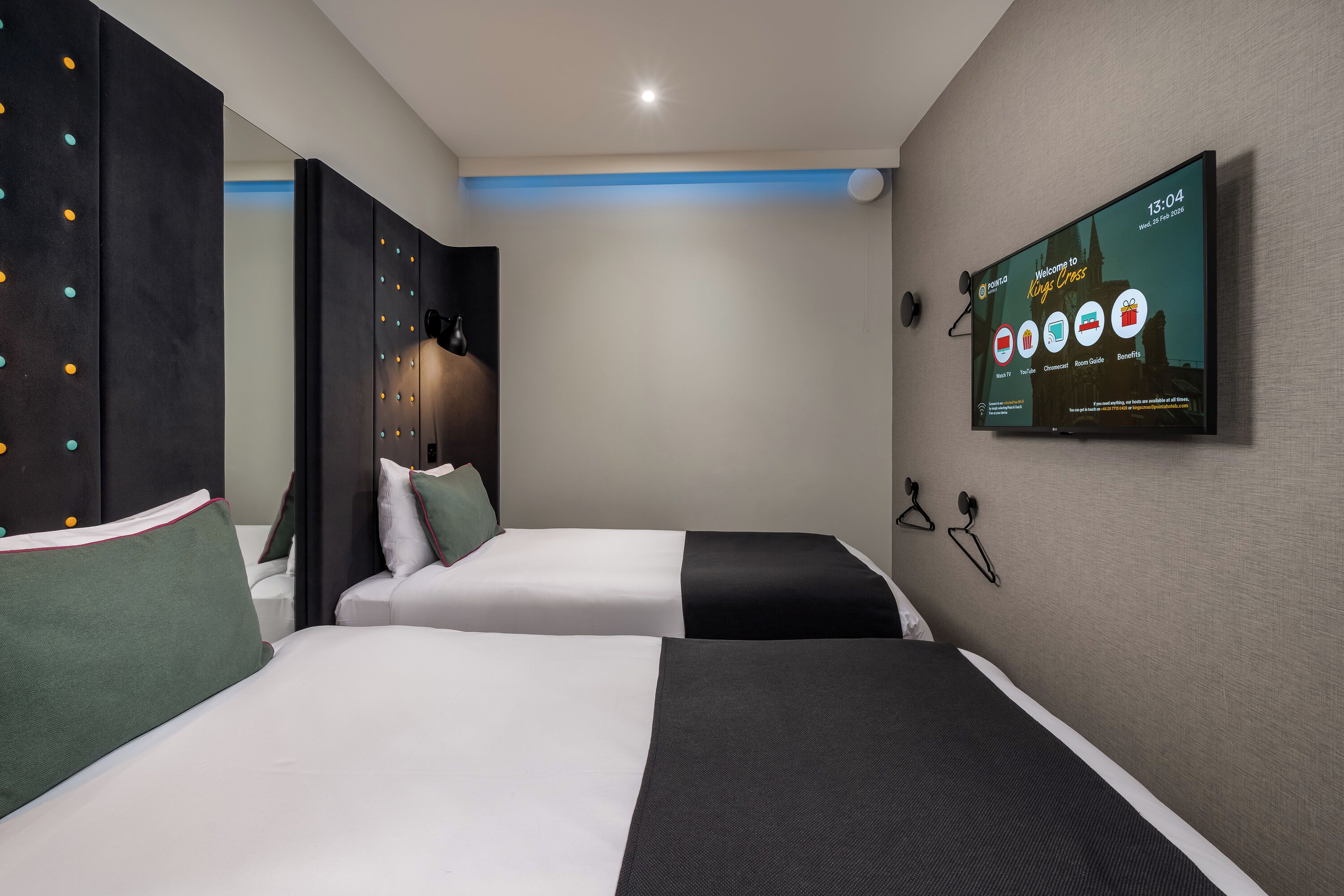 A hotel room with two beds, a TV on the wall, and a view of the city.