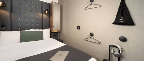 Habitación de hotel moderna con una cama grande, una mesita de noche, una maleta y un perchero en la pared.