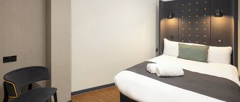 A modern hotel room with a large bed, a chair, and a headboard with lights.