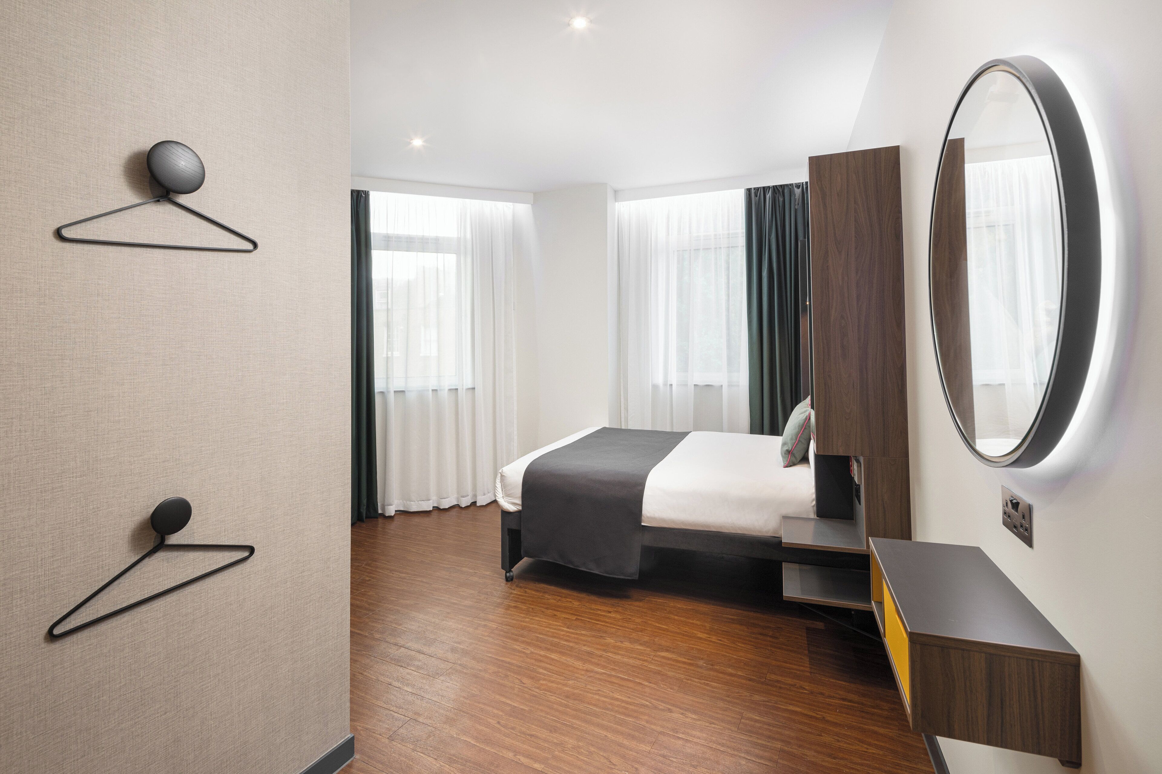 Quarto de hotel moderno com cama bem arrumada, mesa de cabeceira, espelho e luminária fixada na parede.