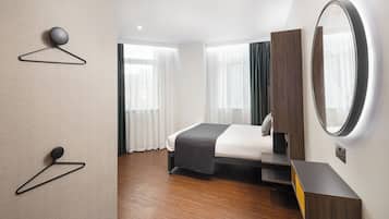 Quarto de hotel moderno com cama bem arrumada, mesa de cabeceira, espelho e luminária fixada na parede.