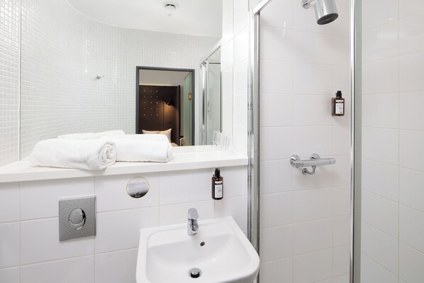 Un baño moderno con lavamanos blanco, un espejo, toallero y zona de ducha.