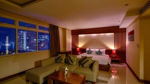 Une chambre d’hôtel avec un canapé, un lit, une table de chevet et une vue sur la ville la nuit.