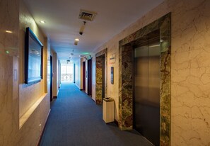 Un pasillo de hotel con paredes de mármol, un ascensor y un cesto de basura.