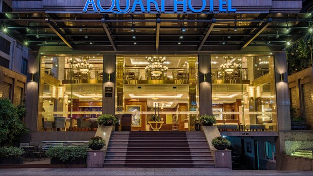 L’extérieur de l’hôtel Aquari se distingue par son imposante entrée, un escalier menant au hall d’accueil et une façade bien éclairée.