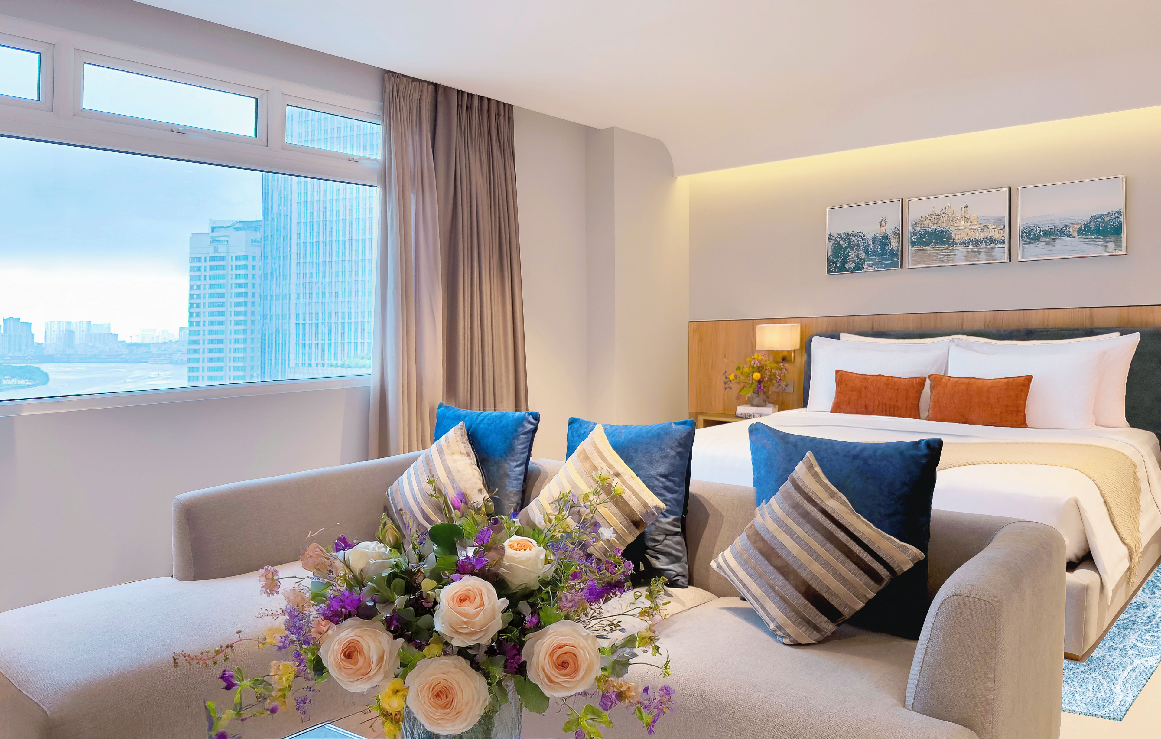 A hotel room with a bed, a sofa, a desk, and a large window with a city view.