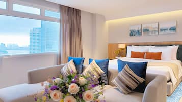 A hotel room with a bed, a sofa, a desk, and a large window with a city view.