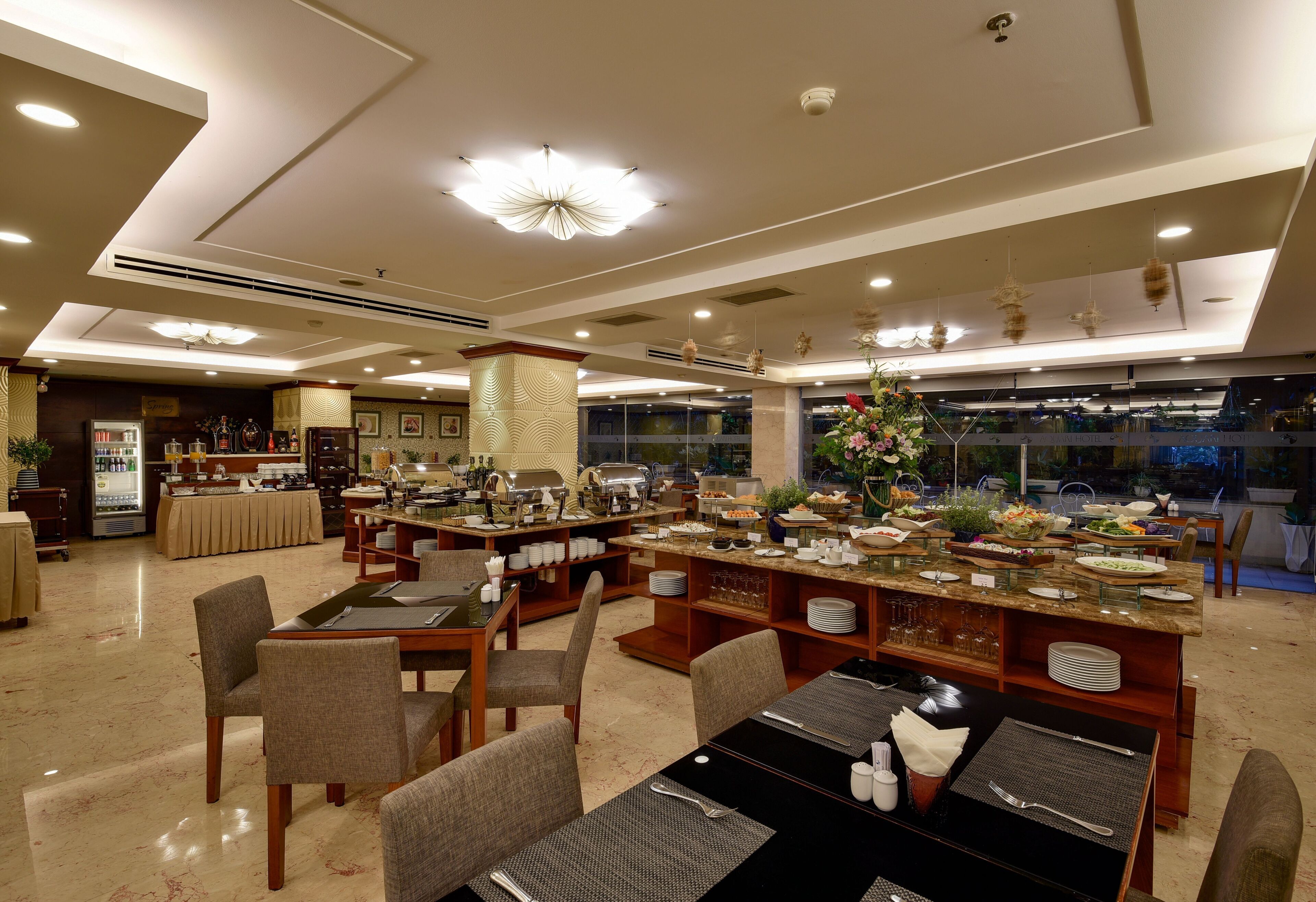 Un ristorante ben illuminato con diversi tavoli e sedie, un'area buffet e un bancone con diversi cibi.
