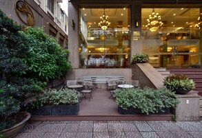 An outdoor seating area with tables and chairs, surrounded by potted plants and a stone-tiled floor.