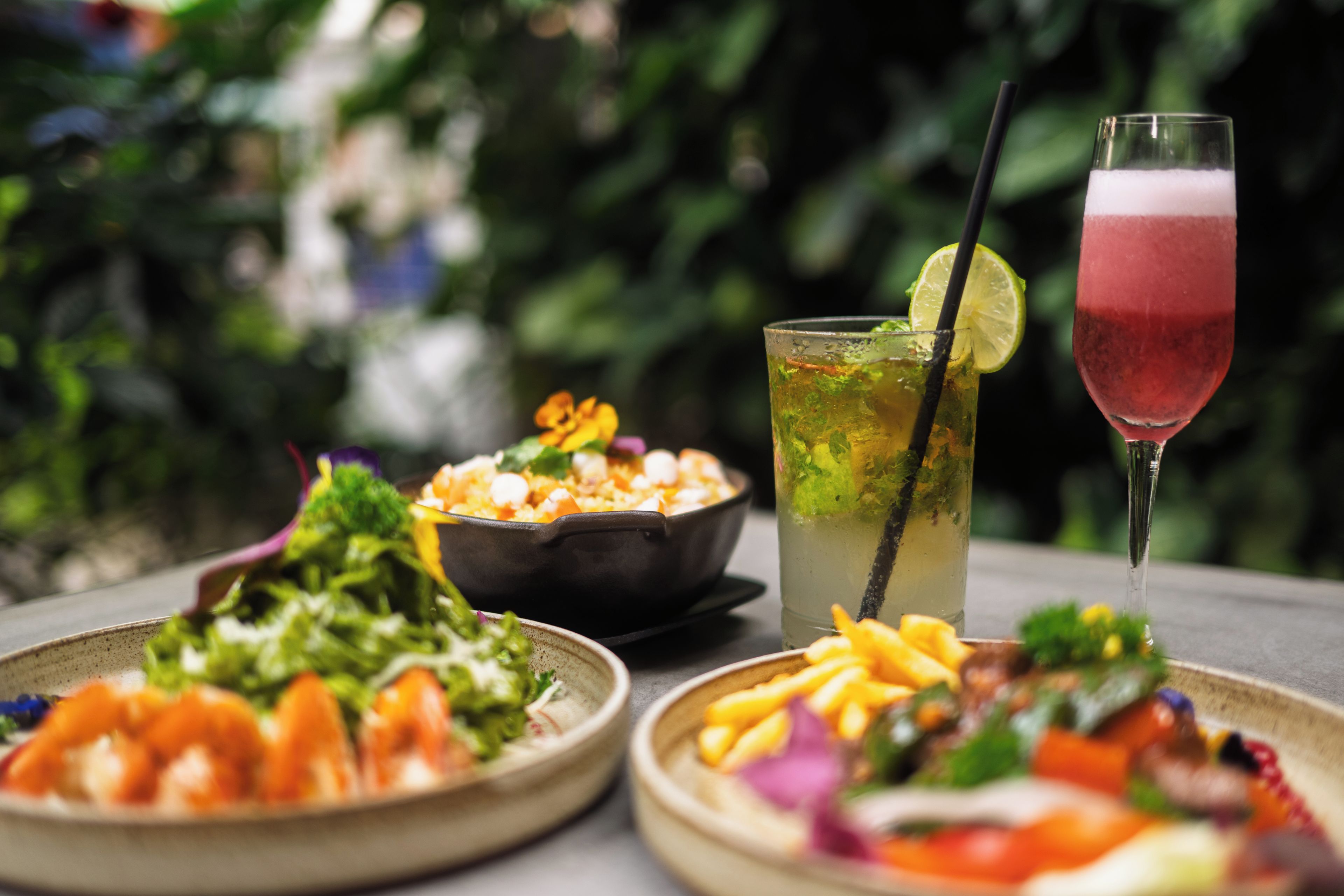 A table set with a salad, a bowl of food, and two drinks.