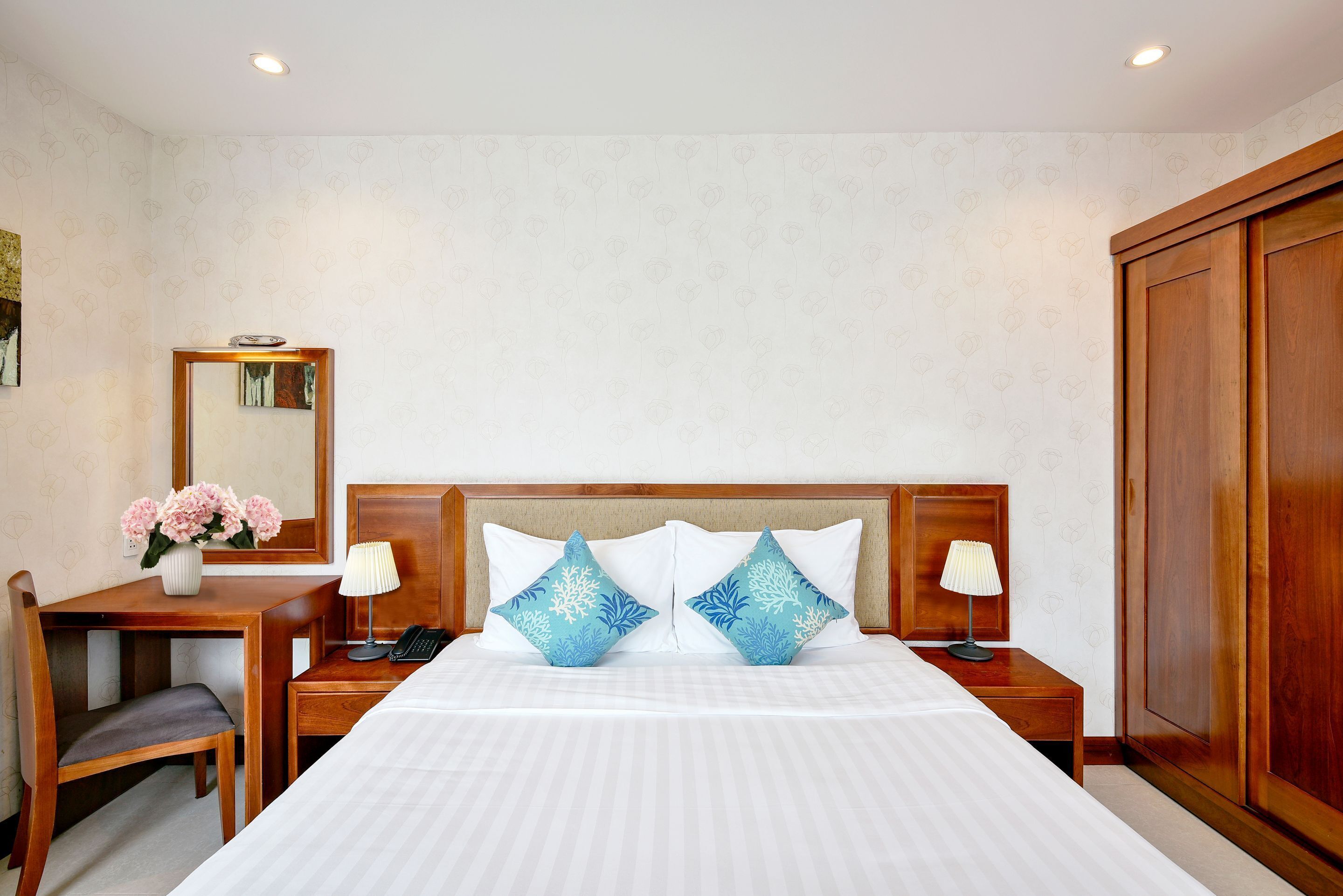 A hotel room with a bed, bedside tables, a desk, a chair, a mirror, and a wardrobe.