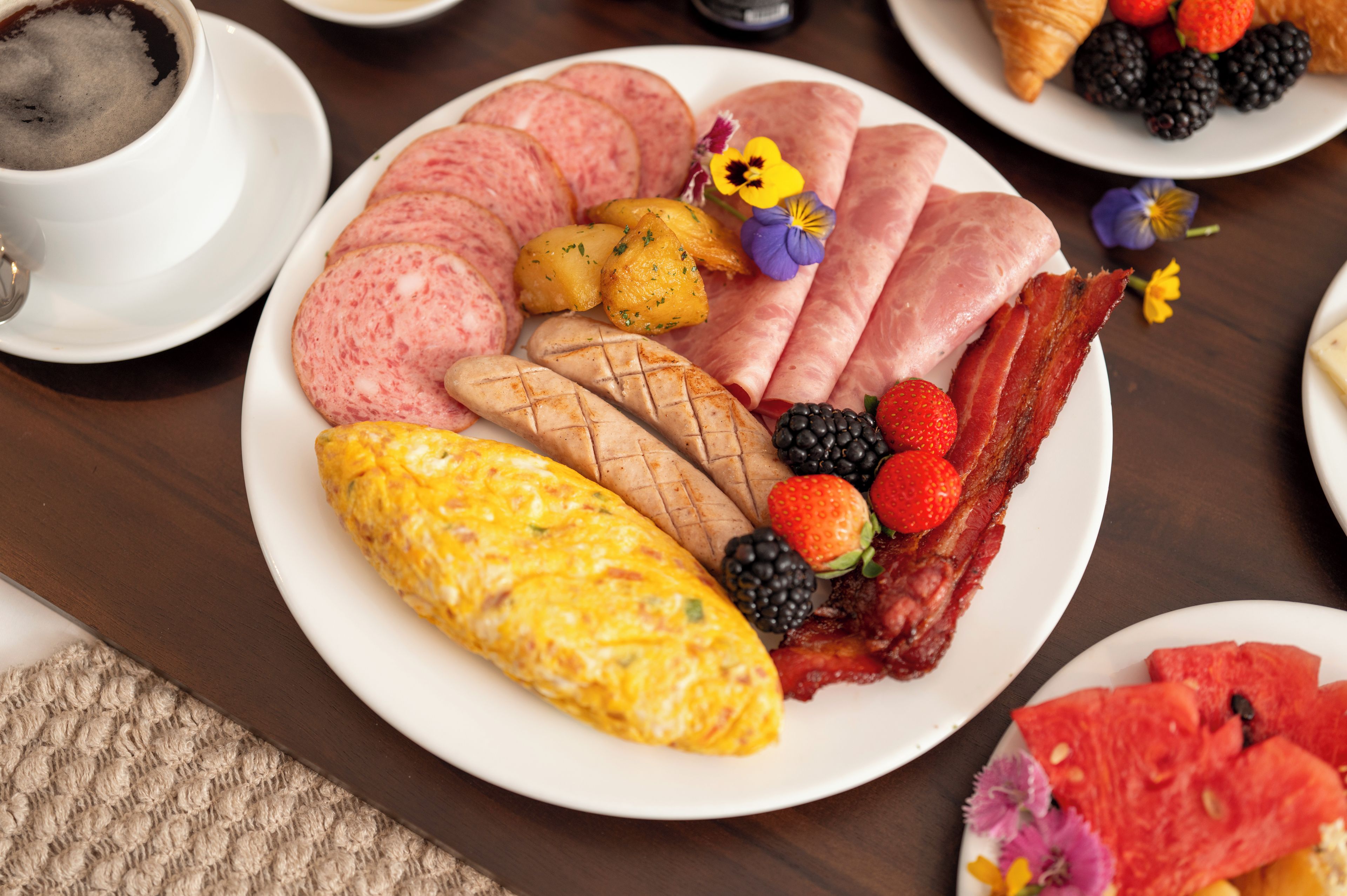 A breakfast plate with ham, eggs, bacon, strawberries, and a croissant.