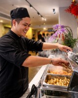 A person serving food from a buffet with multiple dishes visible.