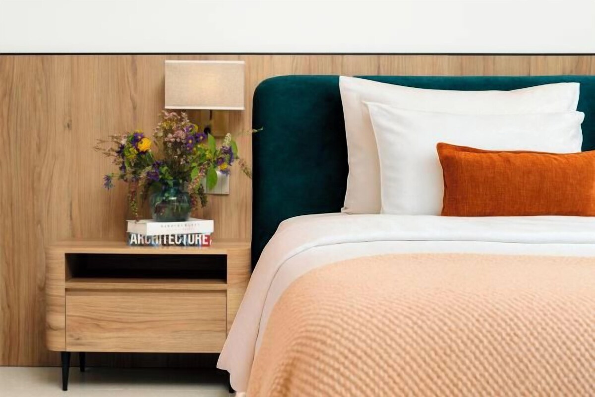 A neatly arranged bedroom with a bed, a nightstand, a lamp, and a vase of flowers.