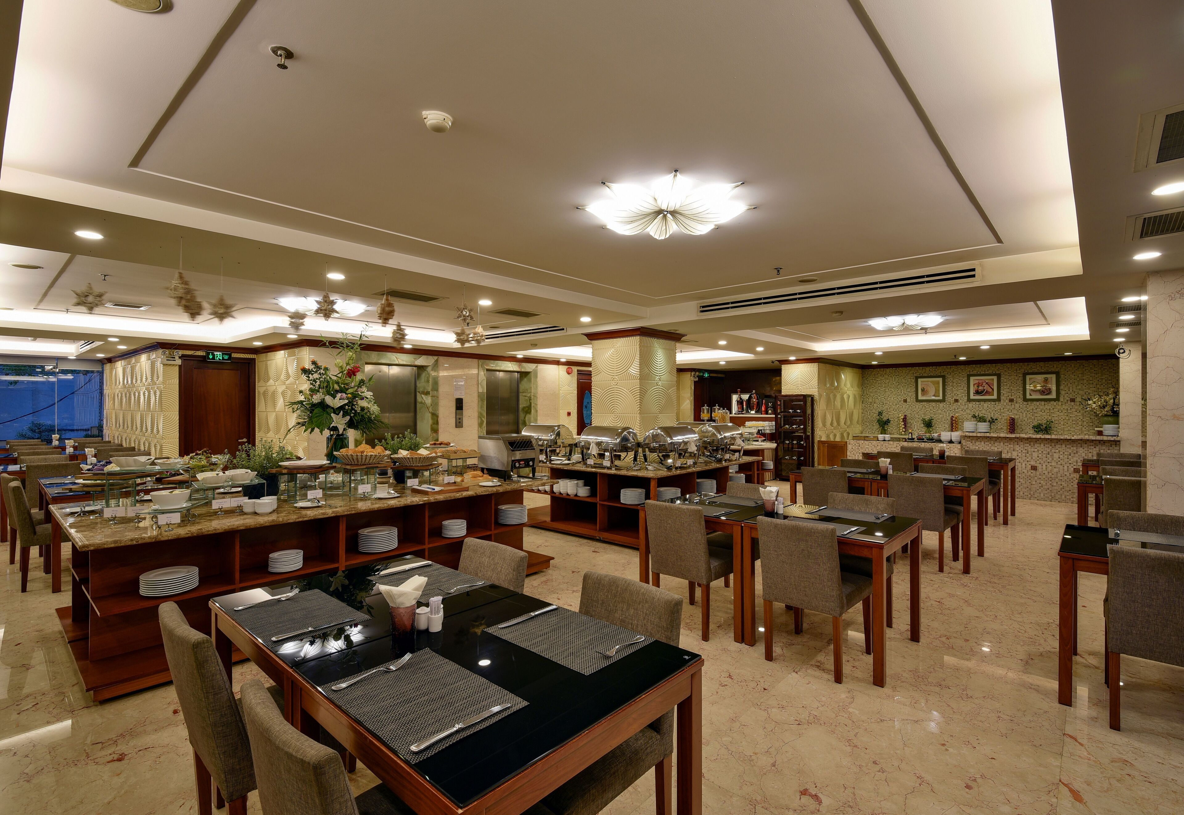 A hotel dining area with multiple buffet stations, seating arrangements, and a reception desk.