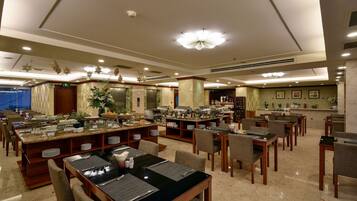A hotel dining area with multiple buffet stations, seating arrangements, and a reception desk.