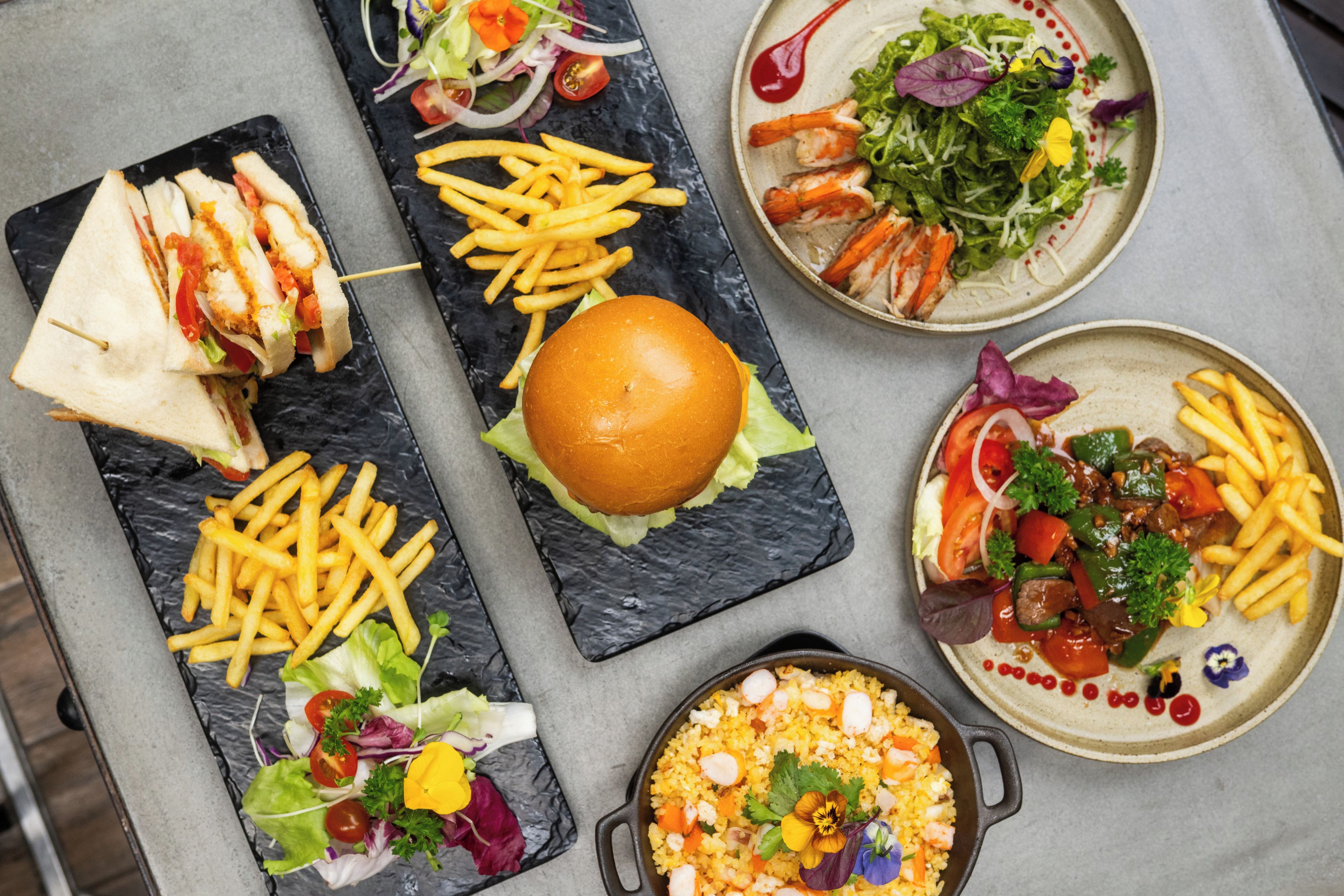 Variedad de platillos que incluyen un sándwich, papas fritas, una hamburguesa y una ensalada.