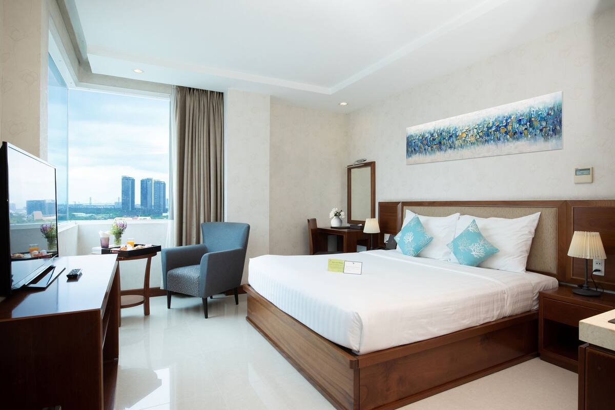 A hotel room with a large bed, a desk with a TV, a chair, a desk lamp, and a painting on the wall.