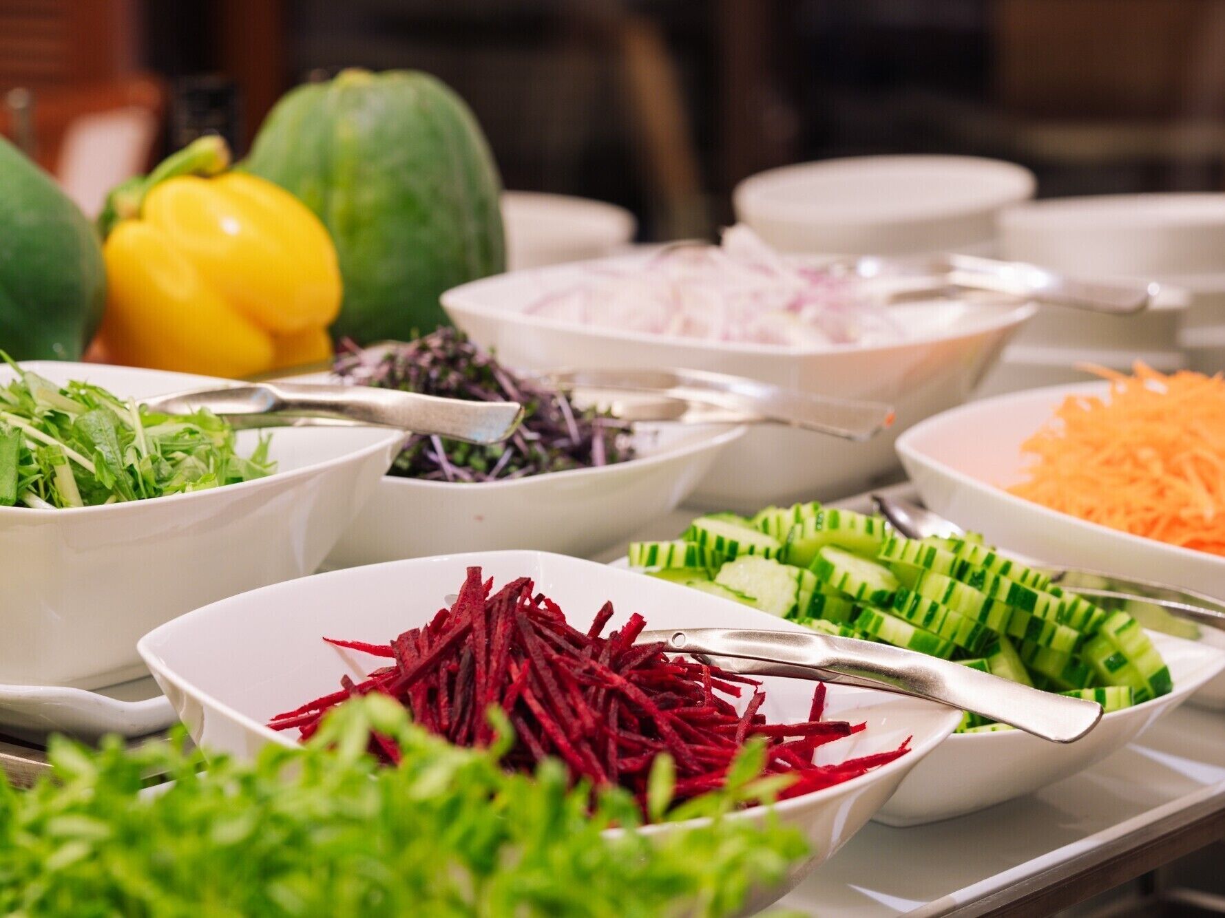 Een buffettafel met diverse gerechten, waaronder salades, gesneden groenten en plakjes komkommer.