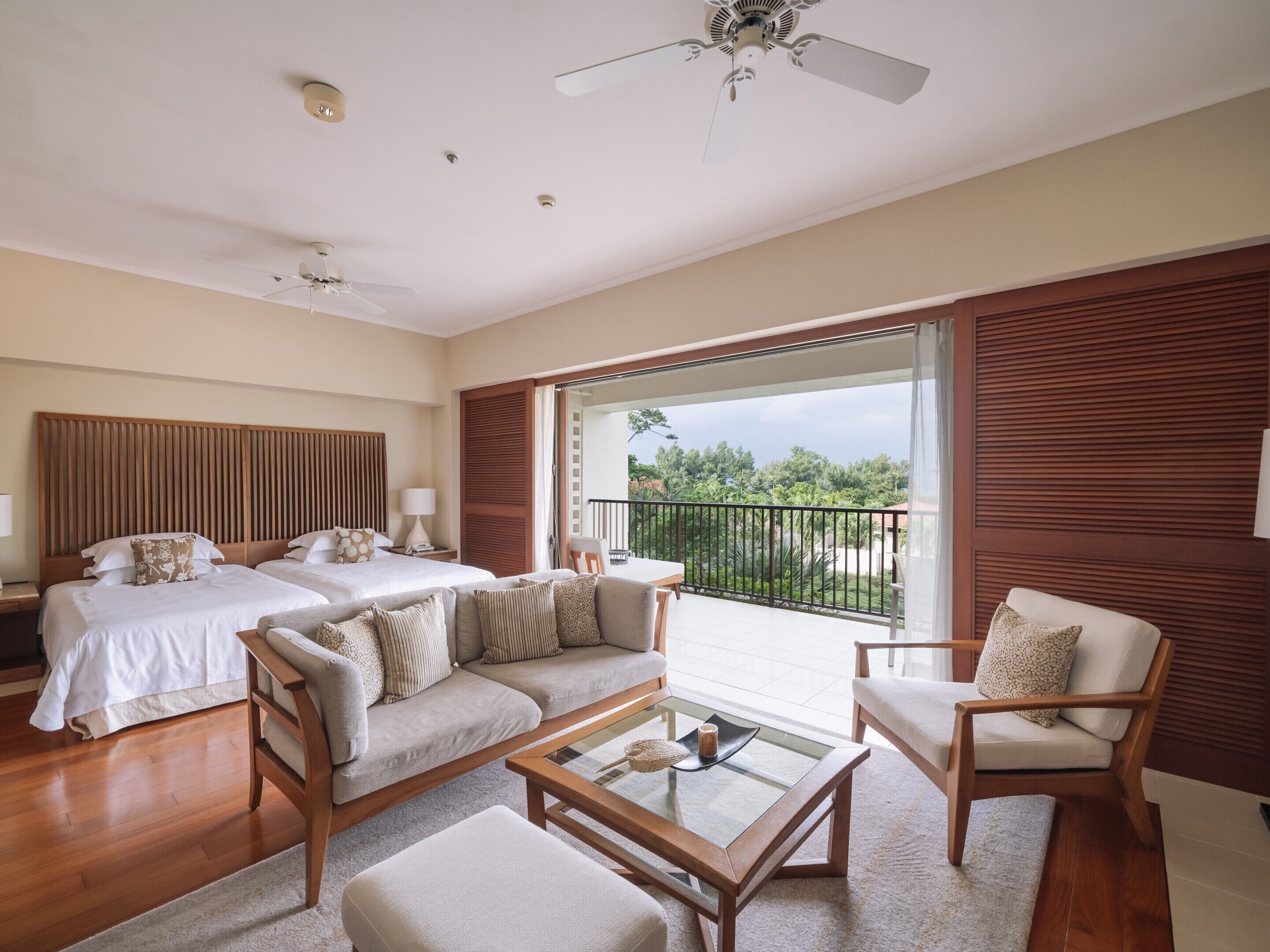 Habitación de hotel con dos camas, un sofá, una mesa de centro y un balcón con vistas.