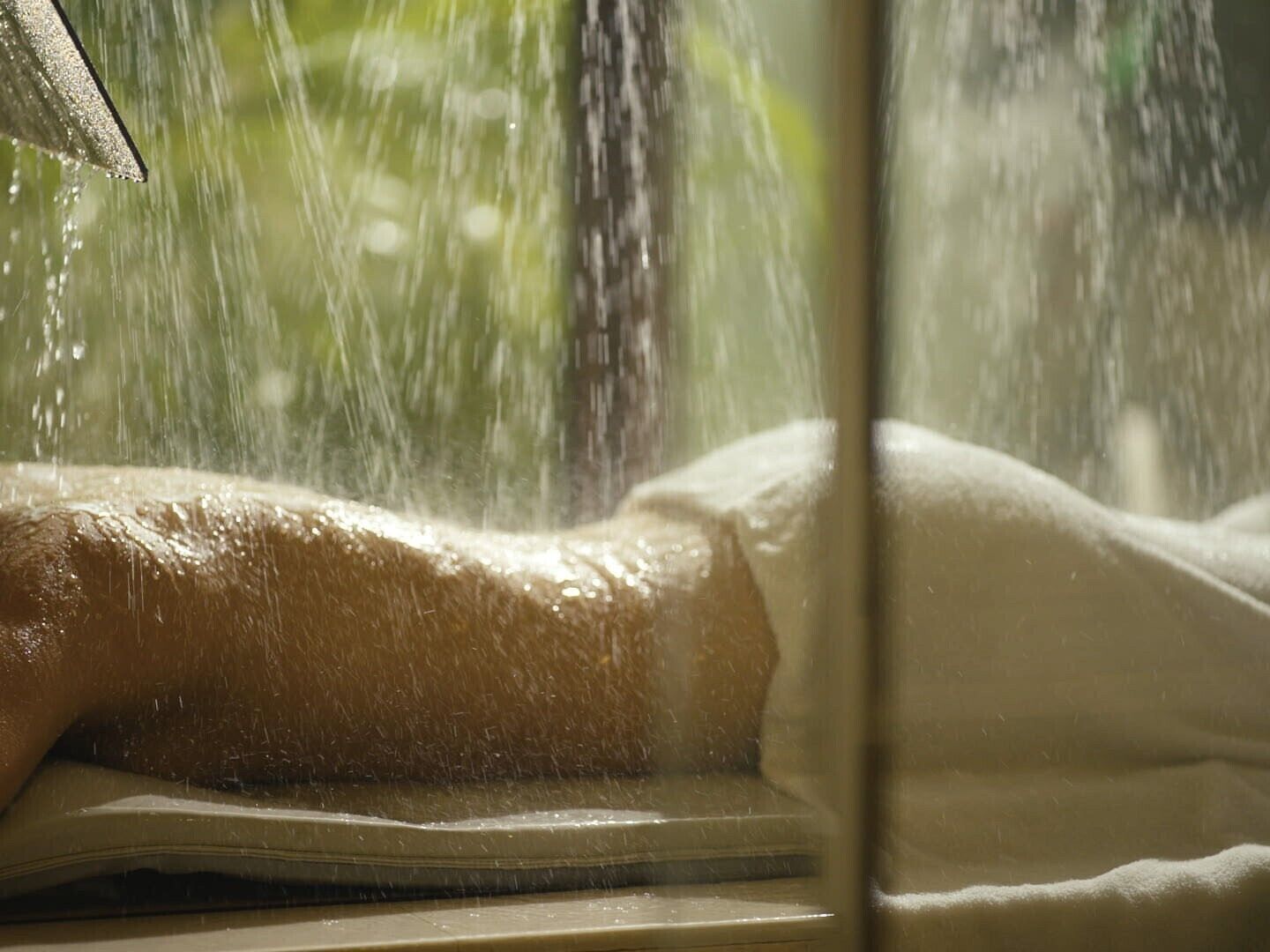 A window with a view of a person lying down, possibly in a bed, with water droplets visible on the window.