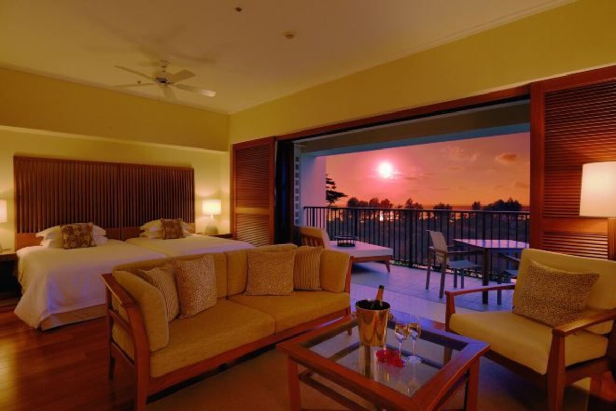 A hotel room with a balcony, a bed, a sofa, and a coffee table.