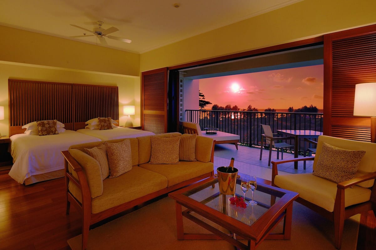 Ein Hotelzimmer mit Bett, Sofa und einem Balkon mit Sonnenuntergangblick.