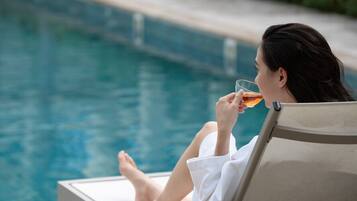 A person relaxing by a poolside lounge chair, holding a glass of a beverage.