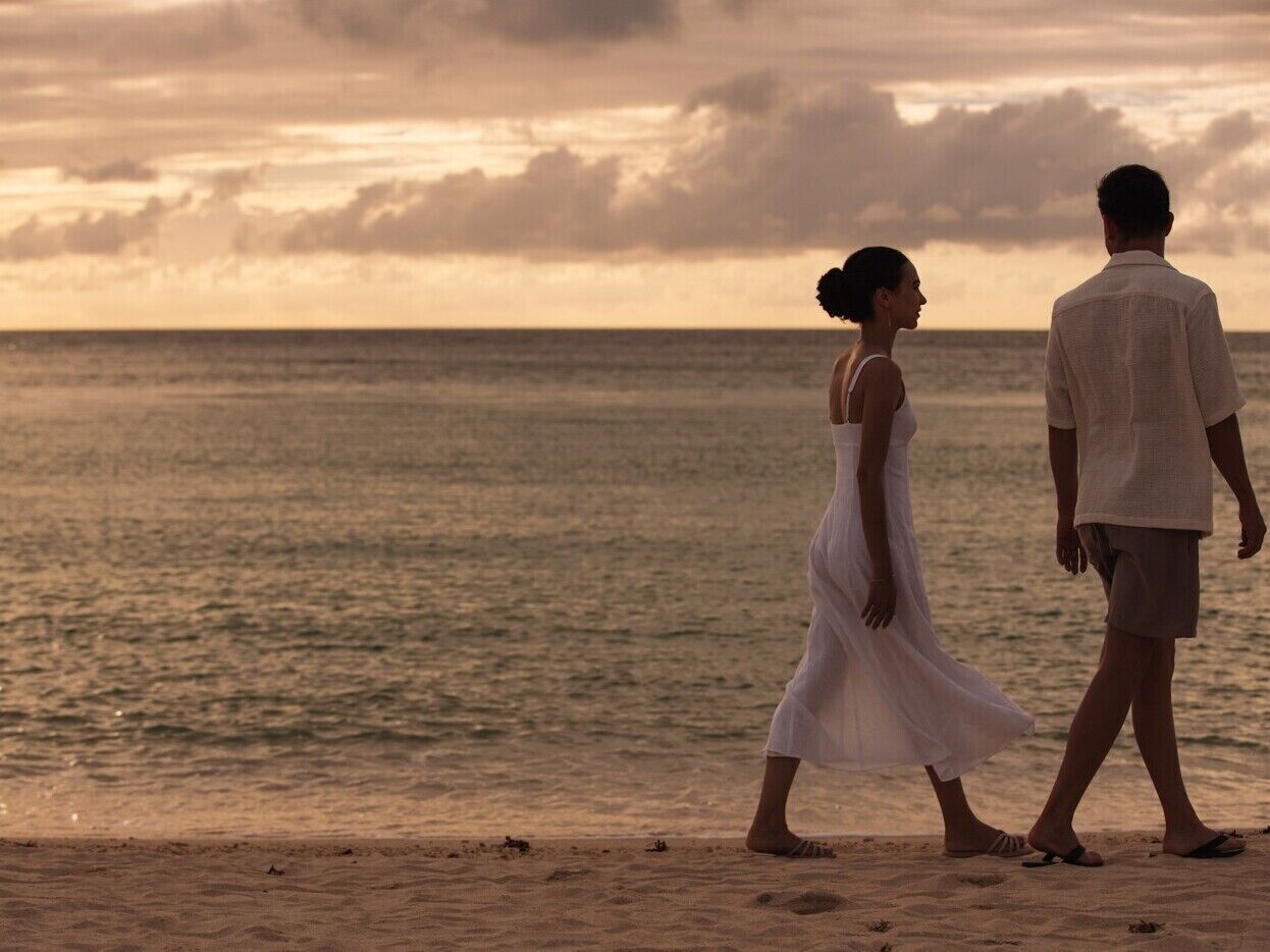 A couple walking on a beach at sunset.
