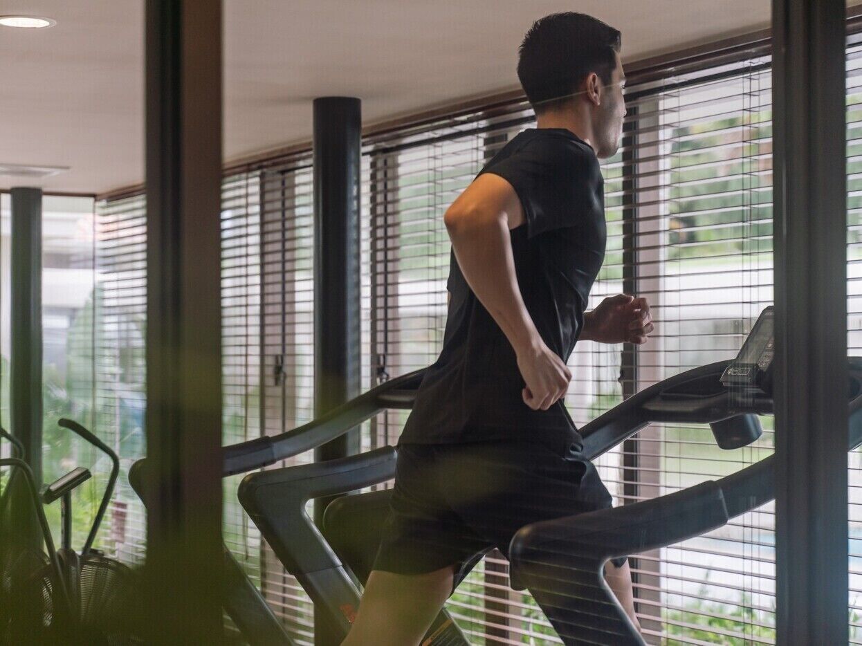 A person running on a treadmill in a room with large windows and a plant in the foreground.