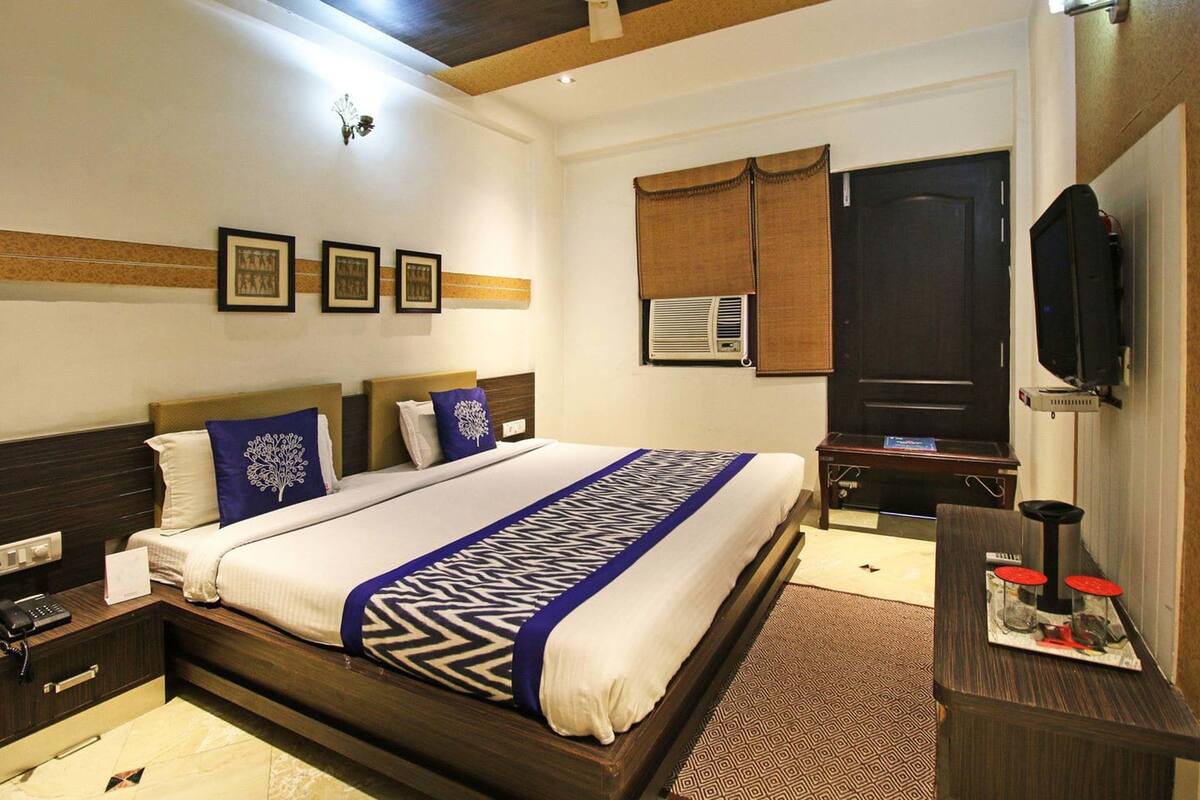 Habitación de hotel con una cama grande, un escritorio con televisor de pantalla plana y una ventana con persianas.