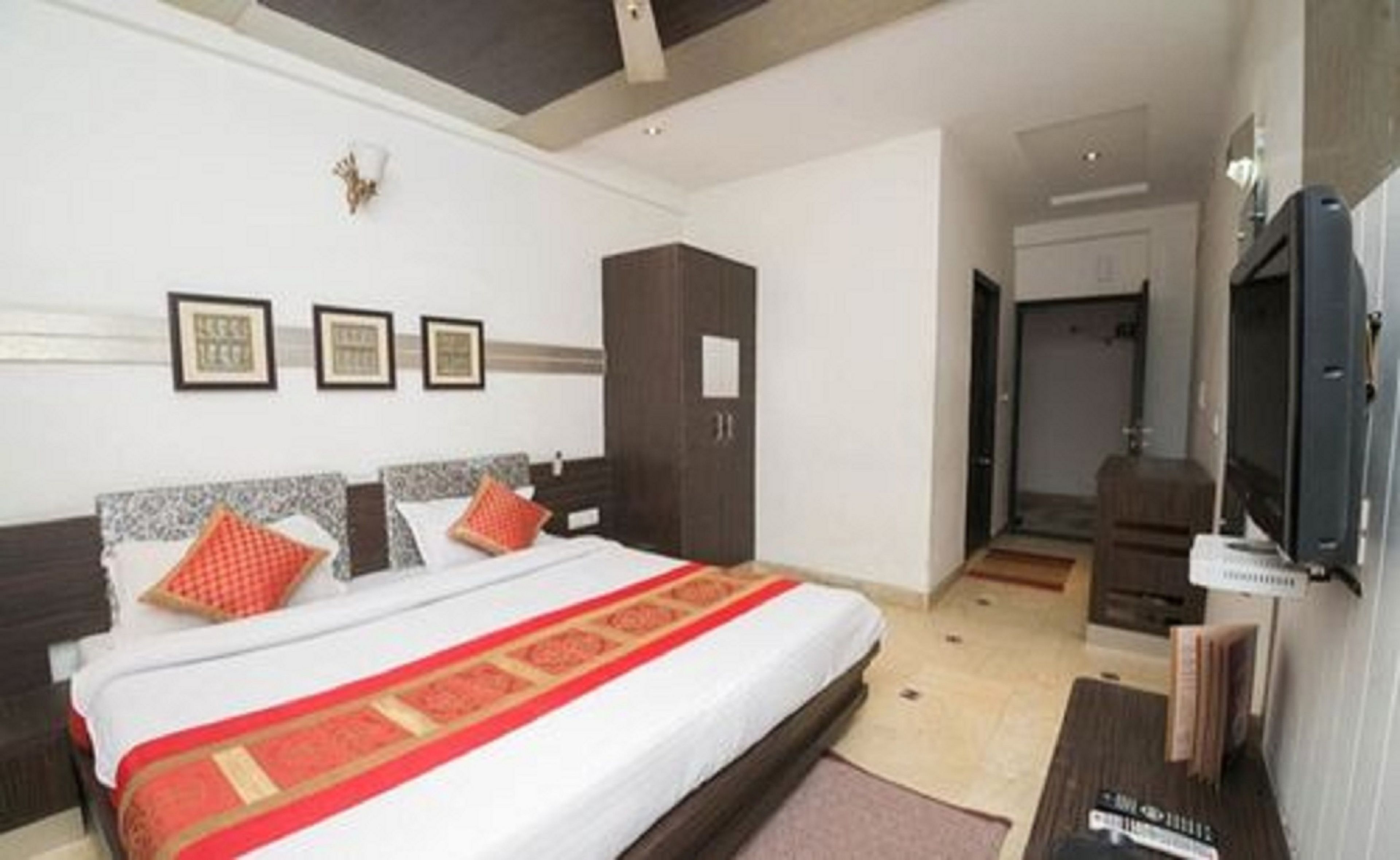 A hotel room with a large bed, a wardrobe, a television, and framed pictures on the wall.