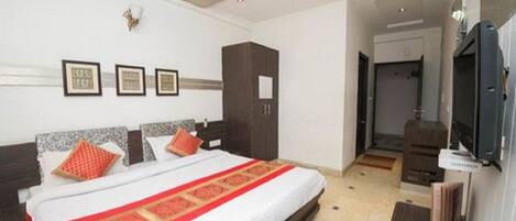 A hotel room with a large bed, a wardrobe, a television, and framed pictures on the wall.