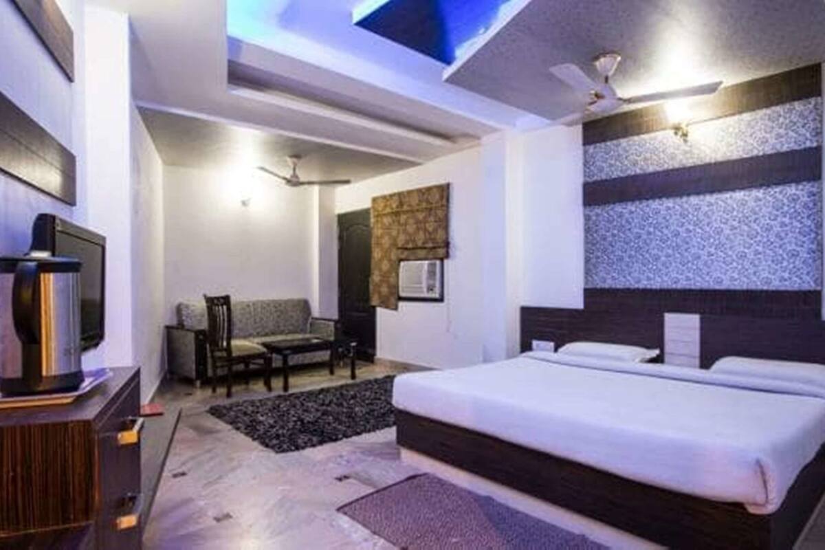 Una habitación de hotel moderna con una cama grande, un escritorio con ordenador, un sofá y un ventilador de techo.